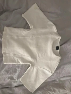 Vit tight topp med kort ärm -  vit topp med tight passform och korta, vida ärmar. Perfekt till jeans eller kjol för en clean look. Rund halsringning och sömdetaljer framtill och baktill.