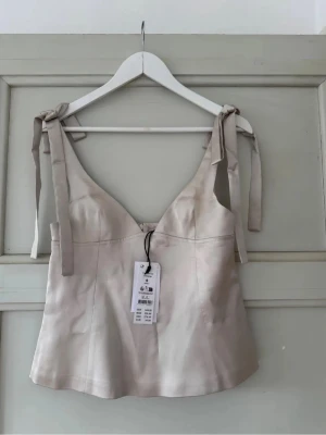 Beige linnetopp med knytband - Säljer denna populära beigea linnetopp med  axelband som knyts i rosetter. Den är från Ginas 14+ i storlek S