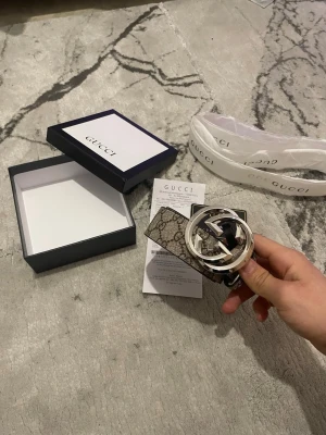 Gucci brunt bälte med GG-mönster - Snyggt bälte från Gucci i brunt skinn med det klassiska GG-monogrammönstret och ett stort, silverfärgat GG-spänne. Perfekt accessoar för att lyfta vilken outfit som helst. Kommer med originalbox och certifikat.