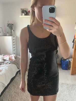 Svart paljettklänning med ärmlös design - Säljer en snygg svart kortklänning med paljetter och ärmlös design. Klänningen har en normal passform och rund halsringning, perfekt till fest, nyår eller glittertema☺️