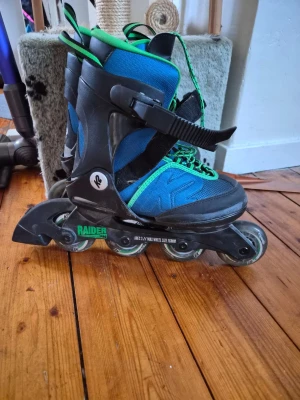 Blåa inlines från K2 Raider - Säljer ett par blåa och svarta inlines från K2, modell Raider. Skydd för handled, armbåge och knä ingår. De har gröna detaljer, snörning och spännen för extra bra passform. Hård plast runt skon ger stabilitet och hjulen är slitstarka för både träning och fritid.