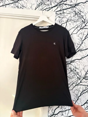 Svart t-shirt från Calvin Klein - Snygg svart t-shirt från Calvin Klein med liten CK-logga på bröstet. Klassisk rund halsringning och korta ärmar. Tillverkad i mjuk bomull för en skön känsla och enkel stil som funkar till allt. Nypris 3 - 400kr mitt pris 250kr