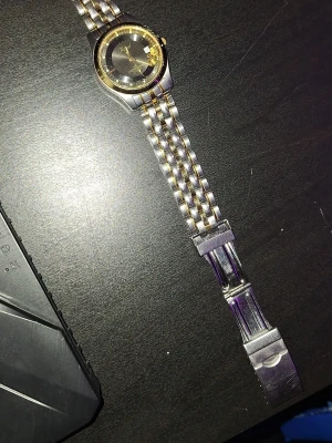 Guld- och silverfärgad klocka från AX - Stilren klocka från Armani Exchange med tvåfärgad länk i guld och silver. Svart urtavla med guldiga detaljer och markerade index. Klassisk design som passar till många outfits. Metallarmband med viklås för säker passform. Trasig men går att fixa enkelt!