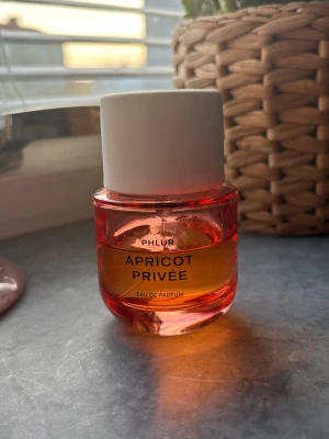 Phlur Apricot Privée Eau de Parfum - En snygg parfymflaska från Phlur med doften Apricot Privée. Flaskan är rundad och har en gradient i orange och rosa glas med vit kork. Modern design som sticker ut på hyllan och passar dig som gillar fruktiga dofter. 50 ml och lite mer än halva flaskan kvar!