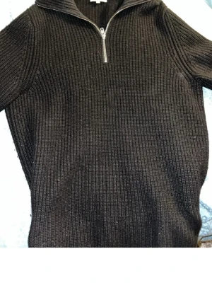 Svart quarterzip stickad tröja Davida Cashmere - Mörk stickad cashmere tröja från Davida i svart med ribbad struktur och halvzip-dragkedja vid halsen. Tröjan har lång ärm och hög krage, perfekt för lager på lager och en clean look. Nypris 2800kr. Passar dig som är runt 175-185 cm lång.