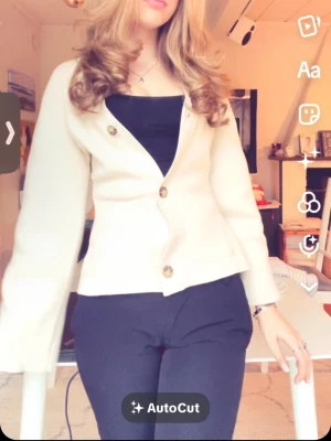 Beige kofta med knappar - Stilren beige kofta med tre stora bruna knappar framtill och lätt utsvängda ärmar. Koftan har ribbade detaljer vid ärmslut och nederkant samt två små fickor framtill. Perfekt att slänga över en topp för en enkel men snygg look.