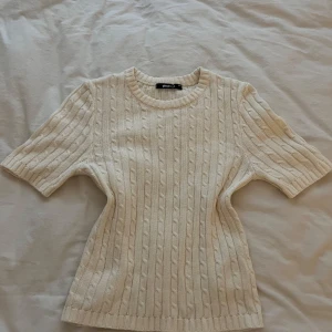 Beige kabelstickad tröja Gina Tricot - Supersöt kabelstickad tröja från Gina Tricot i beige. Tröjan har korta ärmar, rund halsringning och ribbade muddar. Perfekt till jeans eller kjol för en chill och stilren look.