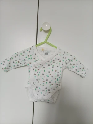 Vit omlottbody med djurmönster Åhléns - Supersöt vit omlottbody från Åhléns i storlek 44/0 mån. Bodyn har långa ärmar och är täckt av små djurmotiv i grått, grönt och brunt. Tillverkad i mjuk bomull som är skön mot huden. Perfekt för de allra minsta!