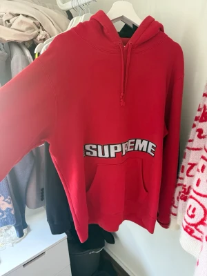 Supreme Blockbuster Hooded Sweatshirt (SS19) - Röd hoodie från Supreme med vit och svart broderad logga över magen och årtalet 2019 på ena sidan. Klassisk känguruficka framtill och justerbar huva med dragsko. Perfekt för dig som gillar streetwear och vill sticka ut.