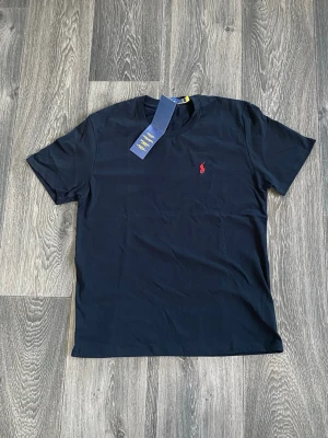 Marinblå t-shirt från Polo Ralph Lauren - Snygg marinblå t-shirt från Polo Ralph Lauren med klassisk röd logga broderad på bröstet. T-shirten har rund halsringning och korta ärmar. Tillverkad i mjuk bomull för skön känsla och stilren look.