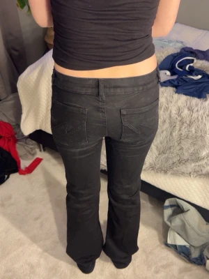 Svarta bootcut jeans med låg midja - Säljer ett par svarta bootcut jeans med låg midja och klassisk femficksdesign. Jeansen har utsvängda ben, perfekta för en avslappnad men trendig look. Materialet är stretchigt denim som sitter snyggt och bekvämt.