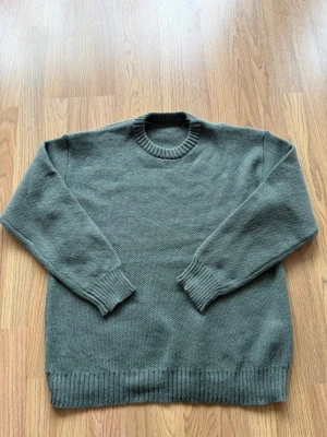 Adrig Använt - En enkel och stilren grågrön stickad tröja med rund halsringning och ribbade muddar vid ärmslut och nederkant. Perfekt för lager på lager och passar till det mesta. Materialet känns mjukt och bekvämt.