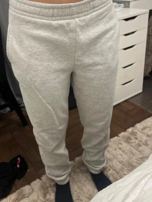 Ljusgrå mjukisbyxor med resårmidja - Säljer ett par ljusgrå mjukisbyxor med resår i midjan och muddar vid bensluten. Byxorna har en avslappnad passform och är tillverkade i mjukt sweatshirtmaterial, perfekta för chill dagar hemma. Klassisk modell utan synligt märke. Smink fläck går inte bort