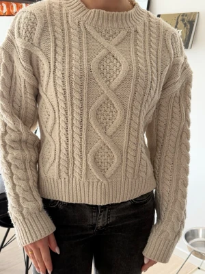 Beige kabelstickad tröja från Lindex - Säljer en beige kabelstickad tröja från Lindex med snygga mönster och struktur. Tröjan har rund halsringning, långa ärmar och ribbade muddar. Perfekt för att hålla sig varm🥰✨