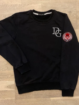 Svart sweatshirt från Dolce & Gabbana - Cool svart sweatshirt från Dolce & Gabbana med DG-logga på bröstet och ett rött broderat märke på ärmen med texten 'King'. Tröjan har rund halsringning, ribbade muddar och är tillverkad i mjukt bomullsmaterial.