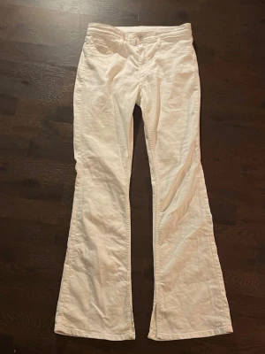 Vita Lågmidjade bootcut jeans - Säljer ett par vita linnebyxor med utsvängda ben och normal passform. Byxorna har klassisk midja, knapp och dragkedja framtill. Perfekta för en avslappnad och stilren look.