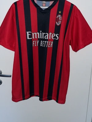 AC Milan matchtröja röd/svart - Säljer en AC Milan matchtröja i rött och svart med vertikala ränder. Tröjan har klubbmärke på bröstet, gul stjärna och sponsortryck 'Emirates Fly Better' framtill. Köptes i Milano äkta kostade ca 1000+