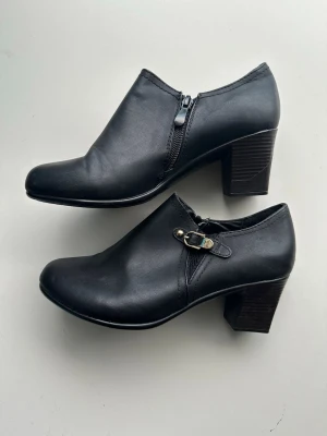 Svarta stövletter med klack, storlek 39 - Superfina svarta högklackade ankelboots / stövletter med lågt skaft i veganskt konstläder. Storlek 39. Snygga till både jeans och klänning, riktigt klassisk modell. Mycket fint skick!  Hämtas i Stockholm eller skickas mot porto.