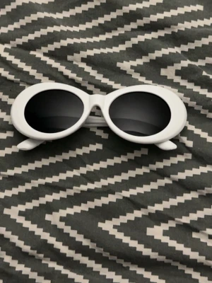 Vita ovala solglasögon retrostil - Säljer ett par vita solglasögon med tjock, oval båge och svarta glas. De har en riktigt retro vibe och passar perfekt för dig som vill sticka ut med din stil. Snygga att matcha med streetwear eller festivaloutfits.