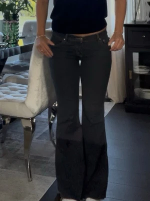 Svarta bootcut jeans med låg midja - Säljer ett par svarta bootcut jeans med låg midja och klassisk femficksdesign. Jeansen har en snygg utsvängd passform från knät och ner, vilket ger en trendig siluett. Perfekta att matcha med crop tops eller stickade tröjor.