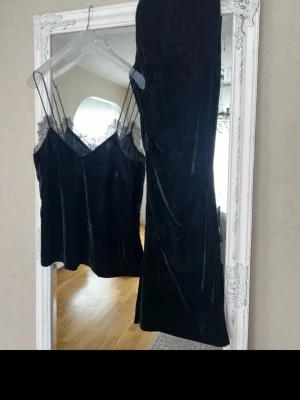 Svart sammets set med spetsdetaljer - Säljer ett svart set i mjuk sammet med linne och matchande byxa. Linnet har tunna axelband och spetsdetaljer vid urringningen för en extra snygg touch. Perfekt för dig som gillar en lyxig och bekväm stil.