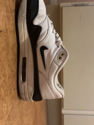 Nike Air Max vita och svarta sneakers - Nike Air Max sneakers i vitt och svart läder med klassisk Swoosh-logga på sidan. Skorna har en synlig Air Max-dämpning i sulan och vita skosnören. Perfekt för dig som gillar sportig och tidlös stil.