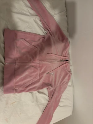 Rosa Juicy Couture hoodie med dragkedja - Säljer en rosa hoodie från Juicy Couture i mjuk velour med dragkedja och huva. På ryggen finns glittrande stenar som bildar texten 'Juicy Couture EST. LOS ANGELES'. Perfekt för en avslappnad och trendig look.