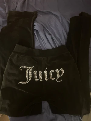 Svarta Juicy Couture mjukisbyxor - Svarta mjukisbyxor från Juicy Couture i velour med glittrande stenar som bildar texten 'Juicy' på baksidan. Byxorna har resår i midjan och klassisk slim fit. Perfekta för en chill och trendig look.