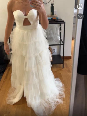 Balklänning - En helt ny balklänning med flera lager volanger i tyll. Klänningen är axelbandslös med hjärtformad urringning och en snygg cut-out framtill. Perfekt för dig som vill ha en vacker klänning med mycket volym. Klänningen är krämvit, mot det vita hållet. 