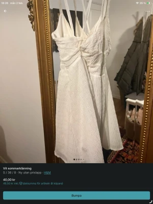 Vit sommarklänning från H&M - Söt vit kortklänning från H&M med smala axelband och snörning framtill. Klänningen har ett diskret rutigt mönster i tyget och är tillverkad i ett lätt bomullsmaterial, perfekt för varma dagar. Den har en feminin passform och omlottdetalj vid bysten.