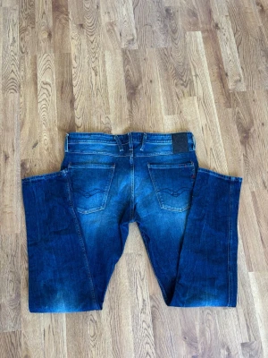 Blå Replay jeans med slitningar - Säljer ett par snygga blå jeans från Replay med klassisk femficksmodell och coola fades. Jeansen har raka ben och tydliga kontrastsömmar. Materialet är denim i bomull och passformen är slim fit. Perfekta för en trendig look.