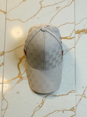 Ljusblå Gcvii keps med monogram - Säljer en ljusgrå keps från Gcci med det klassiska G-monogrammet över hela kepsen. På sidan finns en ikonisk grön och röd rand. Kepsen har böjd skärm och justerbar passform. Perfekt för dig som vill ha en stilren och lyxig accessoar.