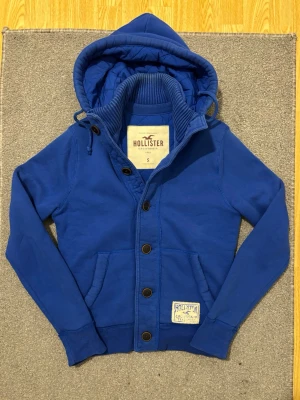 Vintage Hollister Hoodiejacka - Säljer denna feta Hollister hoodiejackan, fodrad inne så varm och skön till det kalla vädret | Väldigt bra skick förutom lite tecken på användning se sista bild | Storlek S | Längd ≈ 65cm, Bredd armhåla - armhåla ≈ 52cm | Modell 175cm, 68kg