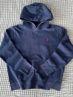 Mörkblå Ralph Lauren hoodie storlek XS-S - Mörkblå Ralph Lauren hoodie med röd logga i 84% bomull och 16% polyester  bra skick, litet slitage på höger arm som inte syns vid användning, lite missfärgad på vissa ställen, annars fräsch  Barnstorlek XL men sitter som någonting mellan XS och S men kolla mått noga Axelbredd: 43 cm Längd: 60 cm