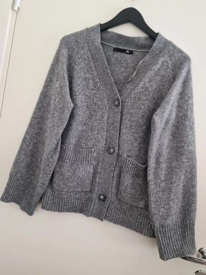 Lager 157 grå kofta med fickor och knappar - Mysig grå kofta med v-ringning och tre knappar framtill. Två stora fickor framtill och ribbade muddar vid ärmslut och nederkant. Perfekt att slänga över en t-shirt för en chill look. Lager 157, storlek L. Fint skick