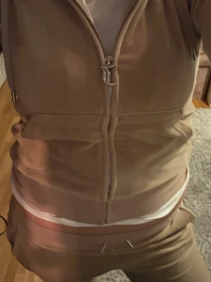 Beige Juicy Couture velourset - Säljer ett velourset från Juicy Couture i färgen Sand med dragkedja på tröjan och strassdetaljer med texten 'Juicy' på både ryggen och byxorna. Setet har en avslappnad passform och är perfekt för chill dagar hemma. Nypris: 2000kr! Pris är diskuterbart 