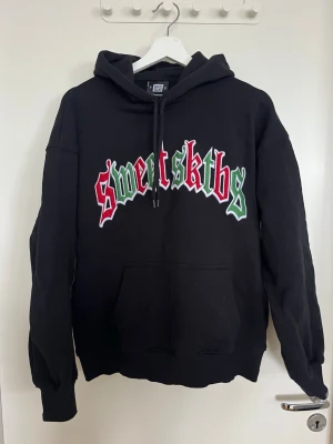 Sweet SKTBS hoodie - Svart hoodie från Sweet SKTBS. Endast använd 1 gång, i väldigt fint skick.  Tjock och skön kvalitet med stort broderat tryck framtill och i unisex modell. Snygg färgkombination som sticker ut lagom mycket mot den svarta basen. 💚🖤❤️