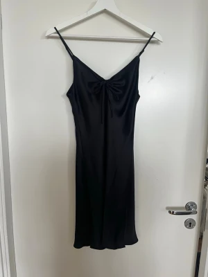 Satin-klänning - Kort svart satin-klänning från BikBok i toppskick (aldrig använd). Smala reglerbara axelband och knytning framtill.  En tidlös modell med snyggt fall som är väldigt lätt att styla efter tillfälle. 🖤