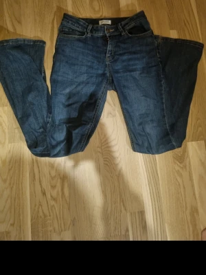 Mörkblå jeans från Lindex Freja - Säljer ett par mörkblå jeans från Lindex i strl 170, modell Freja. Klassisk femficksdesign, flared och normal midja. Jeansen har snygga kontrastsömmar och är tillverkade i ett slitstarkt denimtyg. Perfekta för en avslappnad och trendig look.