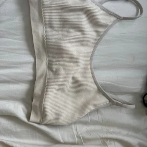 Beige ribbad bralette med smala band - Säljer en stilren beige typ sport bh i ribbat material med smala axelband och bred resår under bysten. Mjuk och stretchig modell utan byglar, perfekt för en avslappnad look. 