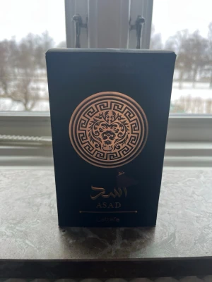 Lattafa Asad parfym 100ml - Lattafa Asad är en parfym i en elegant svart kartong med guldiga detaljer och ett lejonmotiv. Förpackningen har arabiska och engelska texter samt en lyxig känsla. Innehåller 100 ml och har en orientalisk doftprofil. Inte helt full