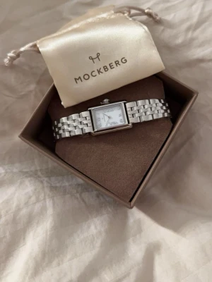 Mockberg silverfärgad armbandsklocka - Stilren armbandsklocka från Mockberg med rektangulärt ur och länkarmband i silverfärgad metall. Urtavlan är vit med romerska siffror och minimalistisk design. Perfekt accessoar för dig som gillar klassisk och modern stil. Varan är helt ny, plast finns fortfarande kvar ( Pris går att diskutera vid snabb affär )