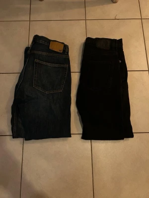 Två par jeans, blå och svarta - Säljer två par klassiska jeans från 157, ett par i mörkblå denim och ett par i svart. Båda har raka ben, femficksmodell och tydliga bakfickor. Perfekta basjeans för dig som gillar enkel och stilren look.