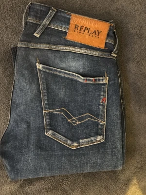 Replay Anbass blå jeans med kontrastsömmar - Snygga blå jeans från Replay med slitna detaljer och kontrastsömmar. Klassisk femficksmodell med Replay-logga på bakfickan och läderpatch i midjan. Jeansen har en modern passform och cool tvätt som ger en avslappnad look. För ändast 500kr