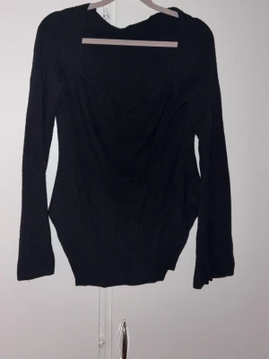 Svart ribbad långärmad topp - Svart ribbad topp med lång ärm och snygg v-ringning. Materialet är stretchigt och sitter skönt mot kroppen. Perfekt att styla med jeans eller kjol för en trendig look.