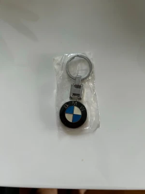 BMW nyckelring i metall - Snygg nyckelring med BMW:s klassiska logga i svart, vitt och blått. Tillverkad i metall med rund form och robust ring för nycklar. Perfekt accessoar för dig som gillar bilar och vill visa ditt intresse för BMW.