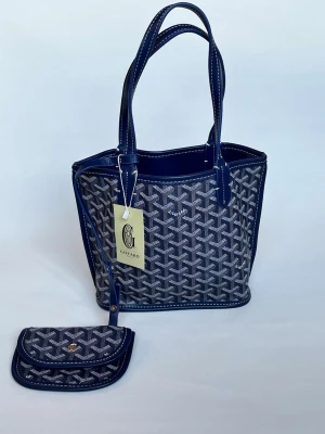 Blå Goyard handväska med mönster - Snygg handväska från Goyard i blått och vitt med det klassiska Goyard-mönstret. Väskan har två handtag, vita kontrastsömmar och kommer med en matchande liten clutch. Tillverkad i canvas med läderdetaljer. Perfekt för dig som gillar exklusiva accessoarer.