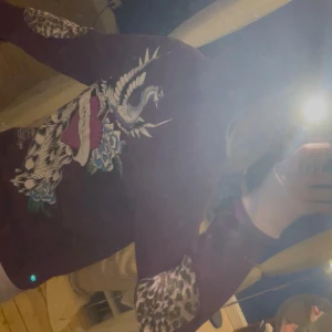 Ed Hardy hoodie med leoparddetaljer - Säljer en mörkrosa hoodie från Ed Hardy med stora tryck framtill och en cool drakdesign på ryggen. Ärmarna har leopardmönstrade detaljer och tröjan har huva med snörning. Mysig varm och cool💕Köpte för 1800 från sellpy och har använt cirka en gång, säljer för att den inte kommer till användning ❤️