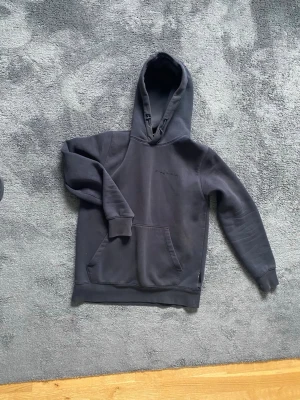 Svart hoodie från Sail Racing - Snygg svart hoodie från Sail Racing köpt från NK i Göteborg  med broderad logga på bröstet. Klassisk modell med stor känguruficka framtill och justerbar huva med dragsko. Nypris 1300.     Tillverkad i mjukt bomullsmaterial som är skönt att bära. Perfekt för en avslappnad och stilren look. Strl S , sparsamt använd.    