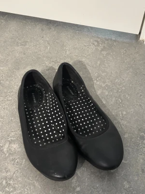 Svarta ballerinaskor från Graceland - Stilrena svarta ballerinaskor från Graceland med rund tå och klassisk design. Skorna har en svart ovandel i syntetmaterial och innersula med vita prickar för en lekfull touch. Perfekta för dig som gillar enkel och tidlös stil.